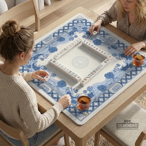 May include: A square wooden table with a blue and white patterned Mahjong mat. The mat features a floral and wave design. Two people are playing Mahjong, with tiles and tea cups visible. The website "DESKNEKO" is printed on the mat.