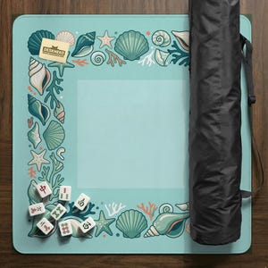 May include: A light blue play mat with a sea life border featuring seashells, starfish, and coral. The mat includes a set of Mahjong tiles and a black carrying case. The Deskneko logo is visible in the corner.