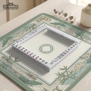 May include: A complete Mahjong set with white tiles featuring red and black characters, arranged on a cream-colored mat with a green floral design. The mat is rectangular with rounded corners and a green border. A small vase and decorative sprig are in the background.