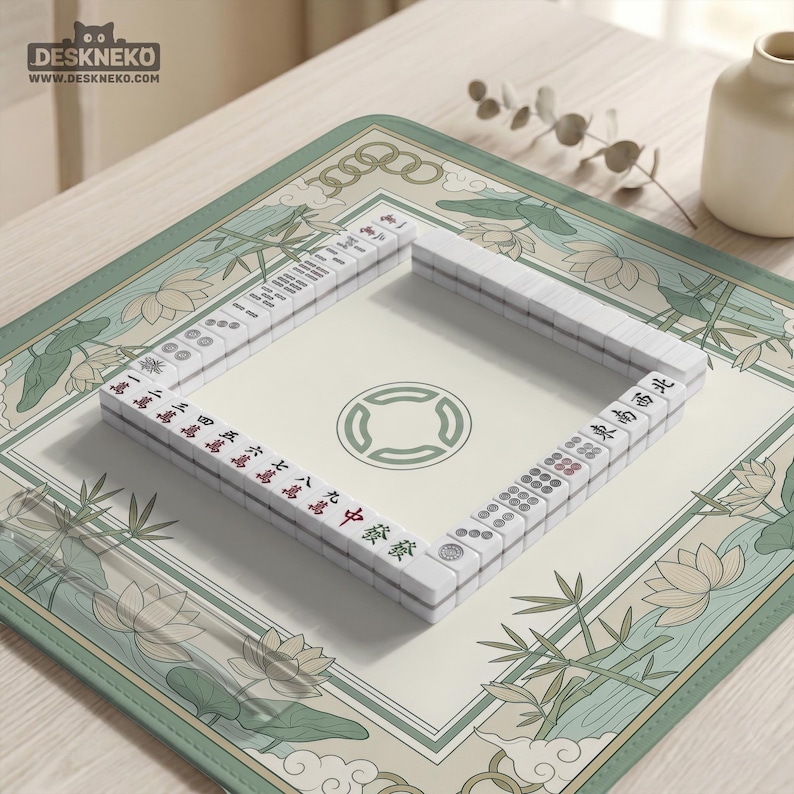 May include: A complete Mahjong set with white tiles featuring red and black characters, arranged on a cream-colored mat with a green floral design. The mat is rectangular with rounded corners and a green border. A small vase and decorative sprig are in the background.