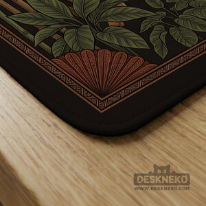 May include: A black desk mat with a detailed botanical design. The mat features green leaves, bamboo stalks, and a fan-shaped element in shades of brown and orange. The border has an intricate geometric pattern. The Deskneko logo is visible in the bottom right corner.