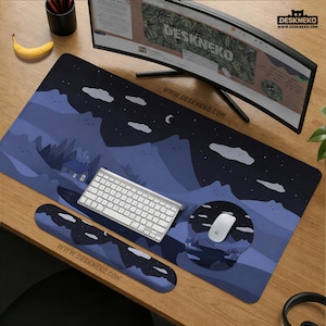 Op de afbeelding: Een bureau-opstelling met een grote blauwe en zwarte bureaumat met een berg- en nachthemelontwerp. Een wit toetsenbord, muis en polssteun liggen op de mat. Het websiteadres www.deskneko.com is afgedrukt.