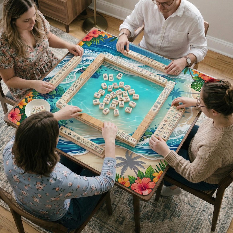 May include: A square mahjong table mat featuring a tropical beach scene with blue ocean waves, palm trees, and red hibiscus flowers. The mat is surrounded by a wooden frame containing ivory-colored mahjong tiles with black and red symbols.