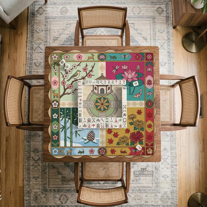 May include: Overhead view of a square wooden table with a colorful Mahjong game mat. The mat features a floral and nature-themed design with a central circular pattern. Four woven chairs surround the table, set on a patterned rug.