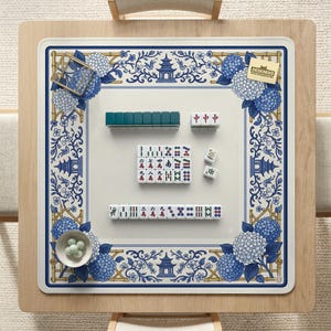 Pode incluir: Um conjunto de mahjong numa mesa de madeira. O conjunto inclui peças, um tapete floral azul e branco e uma pequena tigela com esferas verdes. O tapete tem um design floral azul e branco com o texto "DESKNEKO".