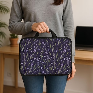 Puede incluir: Una funda para portátil con asa negra y fondo azul oscuro. La funda está decorada con un estampado floral de flores de lavanda y hojas verdes. Las flores son moradas y blancas.
