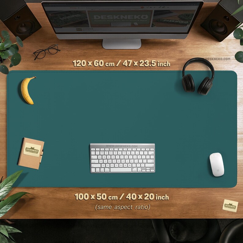 Op de afbeelding: Teal bureaumat met een toetsenbord, muis en koptelefoon. Een banaan en notitieboekje liggen ook op de mat. De mat meet 120 x 60 cm. De website DESKNEKO.COM is zichtbaar.