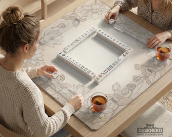 May include: A wooden mahjong table with a floral design mat. The mat features a lotus flower pattern in gray and white. White mahjong tiles are arranged in a square. Two people are playing mahjong, each with a cup of tea.