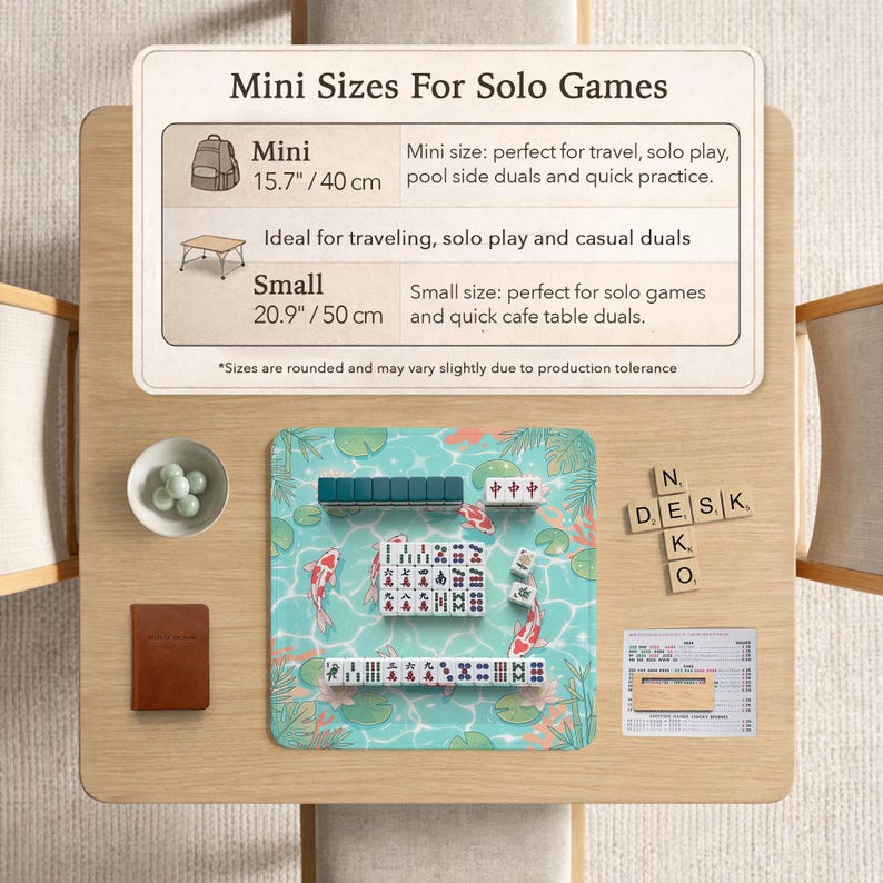 May include: A mahjong set on a light blue mat with koi fish and lily pad illustrations. The mat includes a chart titled Mini Sizes For Solo Games, listing 15.7 inch and 20.9 inch options. Wooden letter tiles spell Neko Desk, with a small bowl of marbles.
