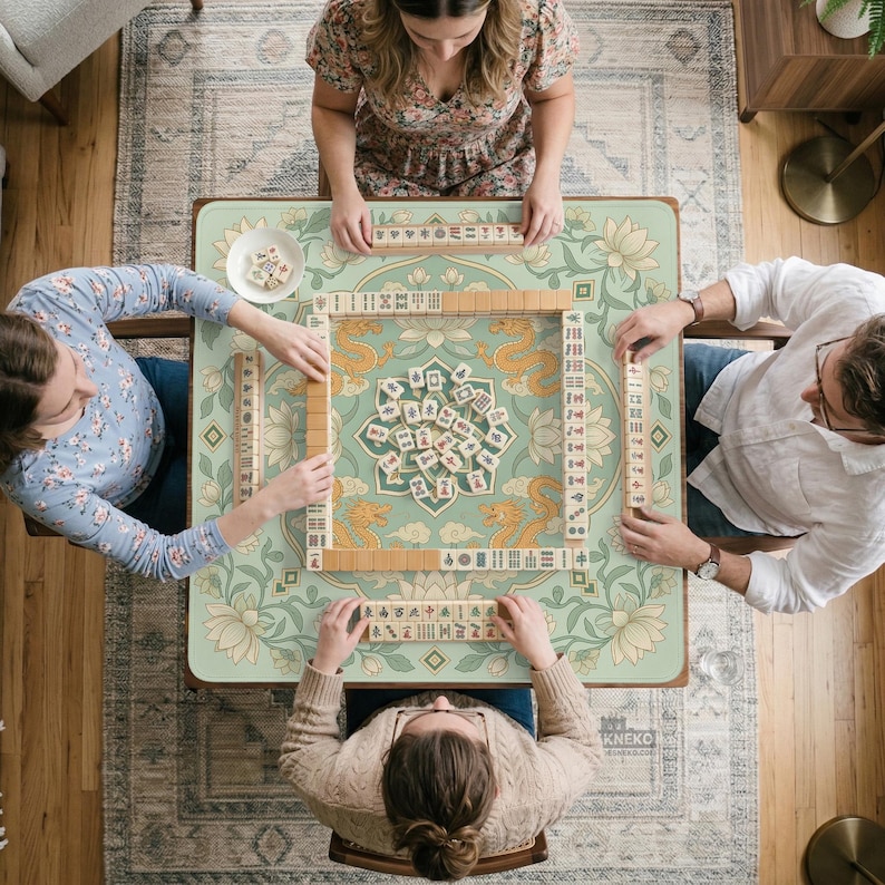 May include: A square mahjong table featuring a light green surface with a central lotus and dragon pattern. The table is set with ivory-colored mahjong tiles arranged in a square perimeter and a central pile, with racks holding tiles for three players.