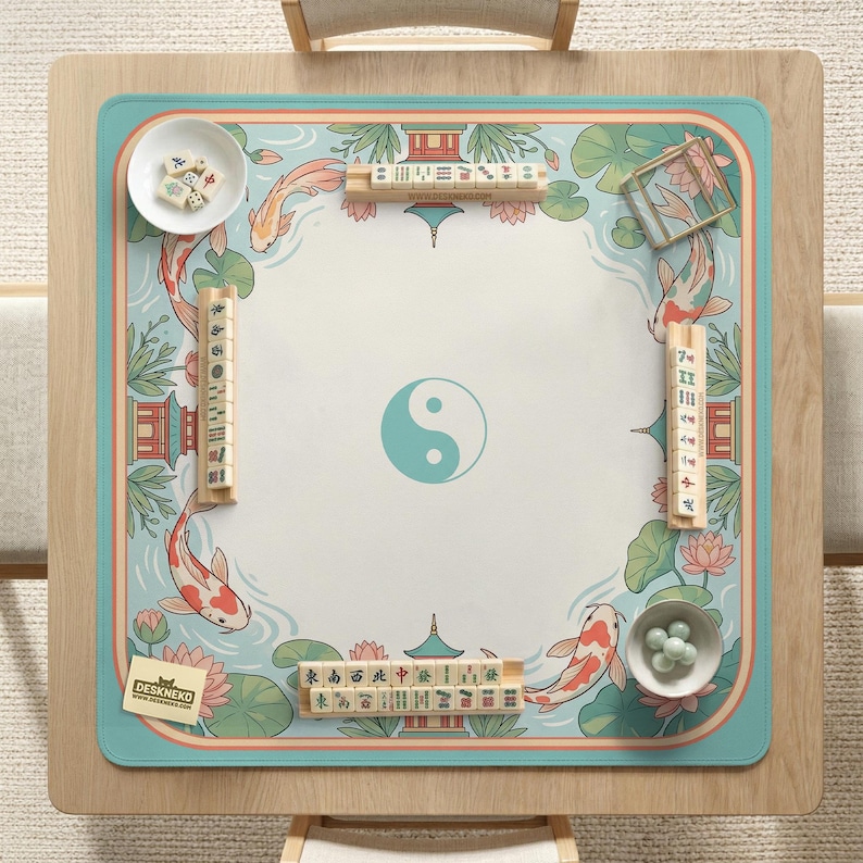 May include: A square mahjong table with a light blue border and a central design featuring a turquoise yin-yang symbol. The table mat has a koi fish and lotus flower design. Includes mahjong tiles and small bowls.