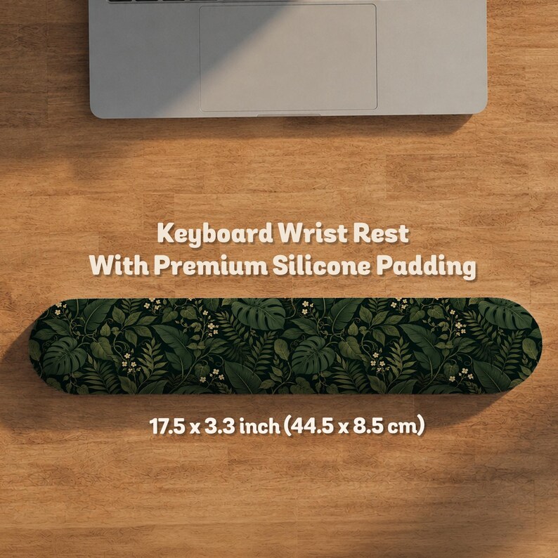 K&ouml;nnte beinhalten: Eine rechteckige Tastatur-Handballenauflage mit Silikonpolsterung und einem dunkelgr&uuml;nen botanischen Muster aus tropischen Bl&auml;ttern und kleinen wei&szlig;en Bl&uuml;ten. Das Produkt misst 44,5 x 8,5 cm und tr&auml;gt den Text Keyboard Wrist Rest.