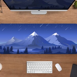 May include: A rectangular mouse pad featuring a mountain landscape under a starry night sky. The design includes snow-capped peaks, a lake, and evergreen trees in shades of blue and white. A computer, keyboard, and mouse are visible.