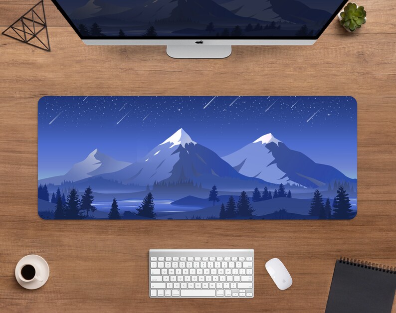 May include: A rectangular mouse pad featuring a mountain landscape under a starry night sky. The design includes snow-capped peaks, a lake, and evergreen trees in shades of blue and white. A computer, keyboard, and mouse are visible.
