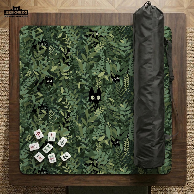 May include: A green and black play mat with a pattern of black cats peeking out from a leafy background. A black carrying case is rolled up next to the mat. Several Mahjong tiles are on the mat.