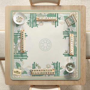 Puede incluir: Una mesa de mahjong cuadrada con un marco de madera clara y una superficie de juego verde y blanca. La superficie presenta bamb&uacute;, flores de loto y patrones de olas. Varias fichas de mahjong, dados y cuencos peque&ntilde;os est&aacute;n dispuestos sobre la mesa. El logotipo "DESKNEKO" es visible.