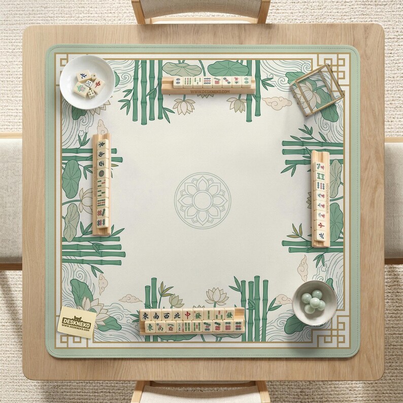 Puede incluir: Una mesa de mahjong cuadrada con un marco de madera clara y una superficie de juego verde y blanca. La superficie presenta bamb&uacute;, flores de loto y patrones de olas. Varias fichas de mahjong, dados y cuencos peque&ntilde;os est&aacute;n dispuestos sobre la mesa. El logotipo "DESKNEKO" es visible.