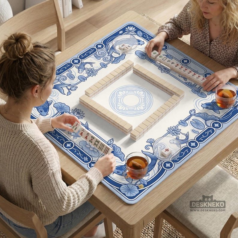 May include: A square mahjong mat featuring a blue and white pattern of koi fish and lotus flowers. The mat has a central circular design and is surrounded by a border of tiles. The text DESKNEKO and a cat icon are printed in the bottom right corner.