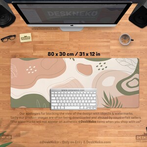 Puede incluir: Alfombrilla de escritorio rectangular, de 80 x 30 cm, con un dise&ntilde;o abstracto en tonos beige, marr&oacute;n y verde. Un teclado blanco est&aacute; encima. El texto "DeskNeko" y una direcci&oacute;n web son visibles.