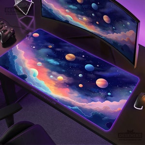 May include: A rectangular gaming mousepad with a vibrant space-themed design. The pad features planets, stars, and colorful nebulae against a dark blue background. The edges are outlined with a purple LED light. The website address "www.deskneko.com" is printed on the pad.
