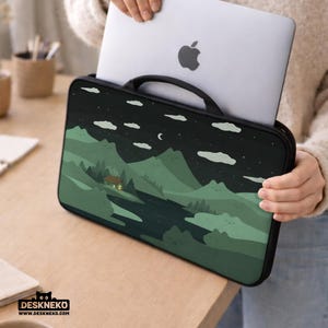 May include: A black laptop sleeve with a handle, featuring a landscape design of mountains, a river, and a cabin under a starry night sky. A silver laptop is partially visible inside the sleeve.