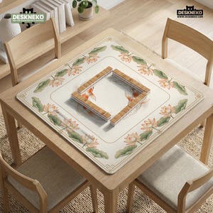 May include: A square table mat with a floral and koi fish design. The mat features a cream-colored background with a border of lotus flowers and green leaves. A wooden frame sits in the center. The table and chairs are made of light-colored wood.