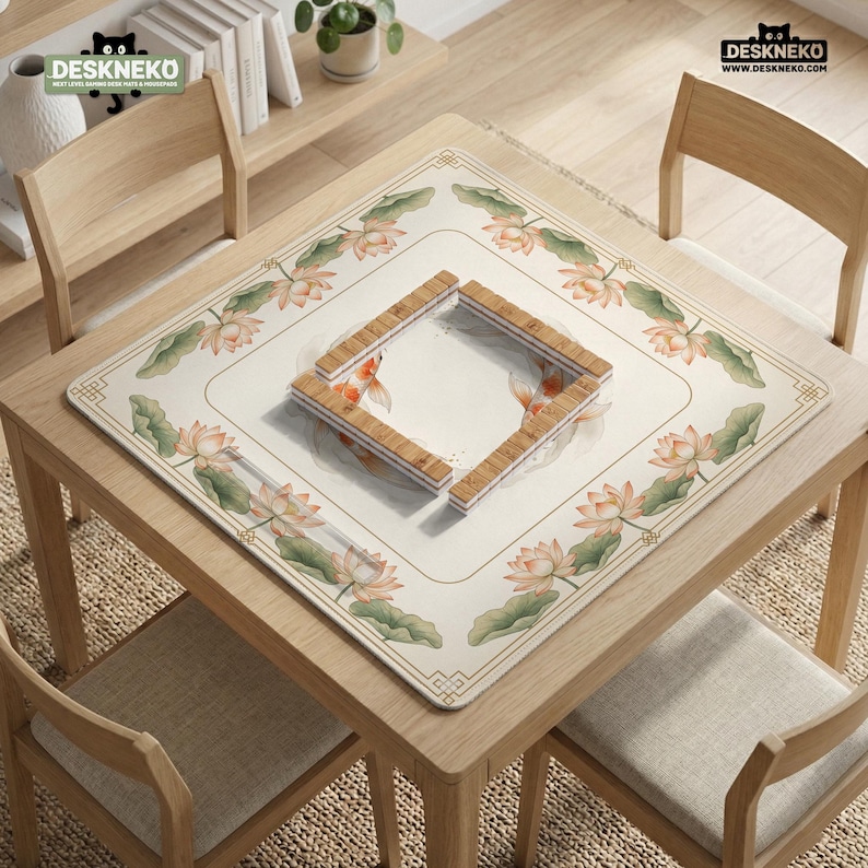 May include: A square table mat with a floral and koi fish design. The mat features a cream-colored background with a border of lotus flowers and green leaves. A wooden frame sits in the center. The table and chairs are made of light-colored wood.
