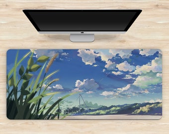 May include: A rectangular desk mat featuring a scenic illustration of a bright blue sky filled with fluffy white clouds. Green grass and foliage are in the foreground. A computer monitor sits above the mat on a light wood surface.