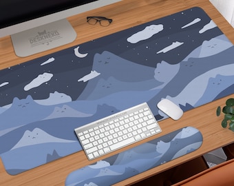 May include: A blue and white desk mat, keyboard, mouse, and wrist rest set. The mat features a mountain range design with cat faces, clouds, and a crescent moon. The keyboard and mouse are silver and white. The wrist rest has a matching design. The website www.deskneko.com is visible.