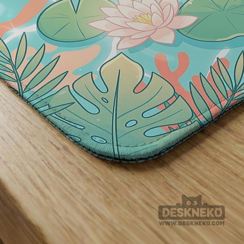 May include: A rectangular desk mat featuring a vibrant illustration of a light blue pond with pink water lilies, green lily pads, and various tropical leaves. The bottom right corner displays the text DESKNEKO and WWW.DESKNEKO.COM.