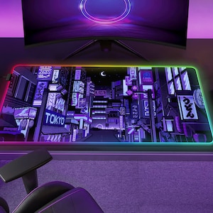 May include: A rectangular gaming mouse pad with a vibrant, pixelated cityscape design, featuring the word "TOKYO" in white. The pad has a glowing, multi-colored LED edge. A computer monitor and gaming chair are visible in the background.