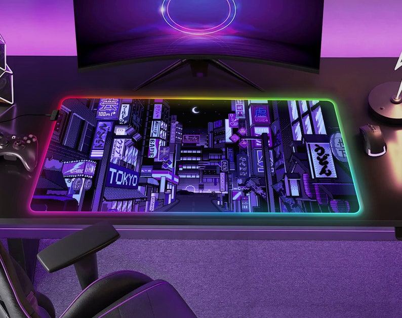 May include: A rectangular gaming mouse pad with a vibrant, pixelated cityscape design, featuring the word "TOKYO" in white. The pad has a glowing, multi-colored LED edge. A computer monitor and gaming chair are visible in the background.