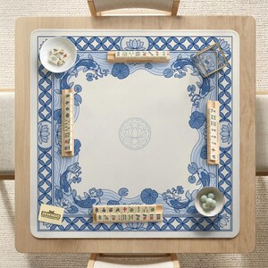 May include: A square wooden mahjong table with a blue and white patterned mat featuring koi fish and lotus flowers. The table is set with tiles, dice, and small bowls. The mat has the text "DESKNEKO".