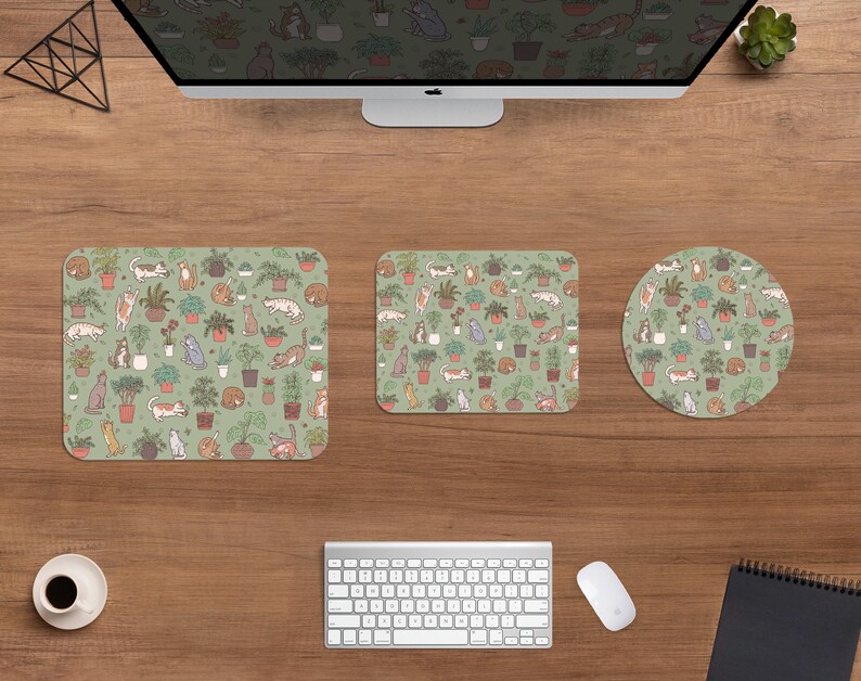 Puede incluir: Una configuraci&oacute;n de escritorio de computadora con un monitor, teclado, rat&oacute;n y accesorios de escritorio a juego. Los accesorios incluyen una alfombrilla de rat&oacute;n cuadrada, un tapete de escritorio rectangular y un posavasos redondo, todos con un patr&oacute;n repetido de gatos y plantas en macetas sobre un fondo verde.
