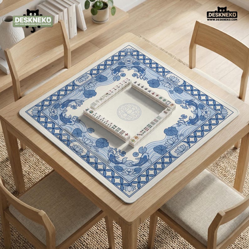 May include: A square mahjong table mat with a blue and white koi fish design. The mat is on a wooden table with a mahjong set in the center. The mat has a floral border and the text "DESKNEKO" in the top corners.