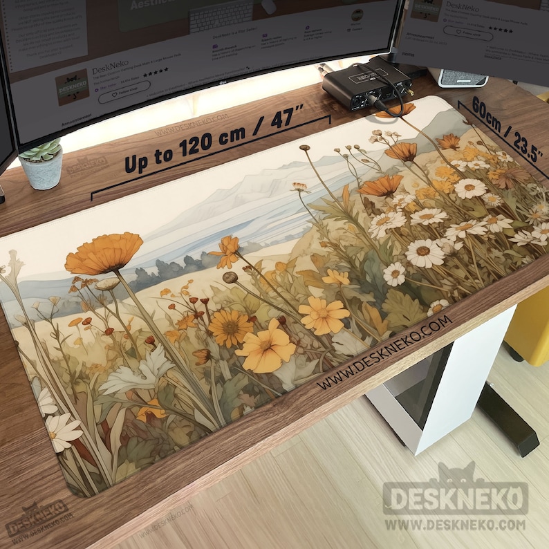 May include: A rectangular desk mat featuring a watercolour design of wildflowers in yellow, orange, and white, set against a backdrop of rolling hills. The mat is up to 120 cm long and 60 cm wide, with the text "DeskNeko" and "www.deskneko.com".