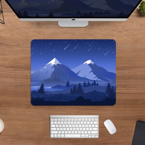 May include: A rectangular mousepad featuring a mountain landscape under a starry night sky. The design includes snow-capped peaks, a lake, and evergreen trees in shades of blue and white. The mousepad is on a wooden desk with a computer, keyboard, and mouse.