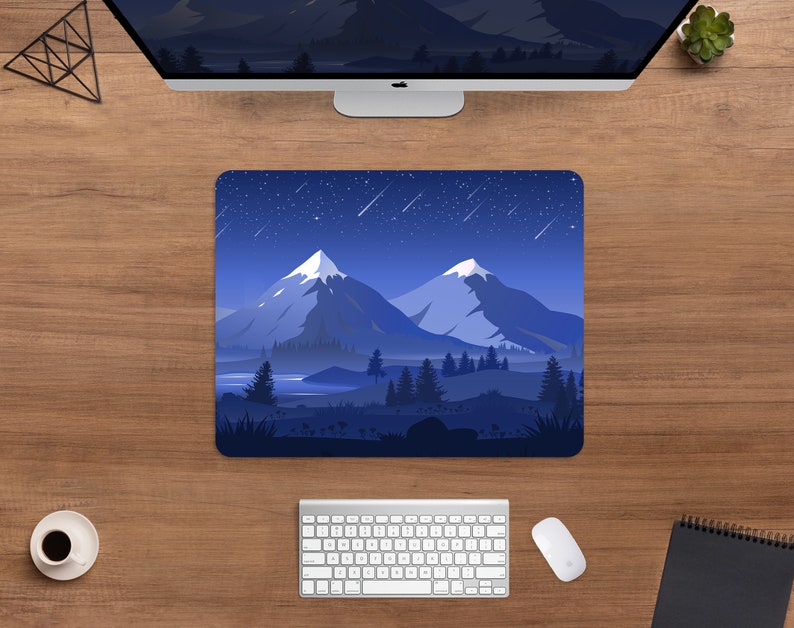 May include: A rectangular mousepad featuring a mountain landscape under a starry night sky. The design includes snow-capped peaks, a lake, and evergreen trees in shades of blue and white. The mousepad is on a wooden desk with a computer, keyboard, and mouse.