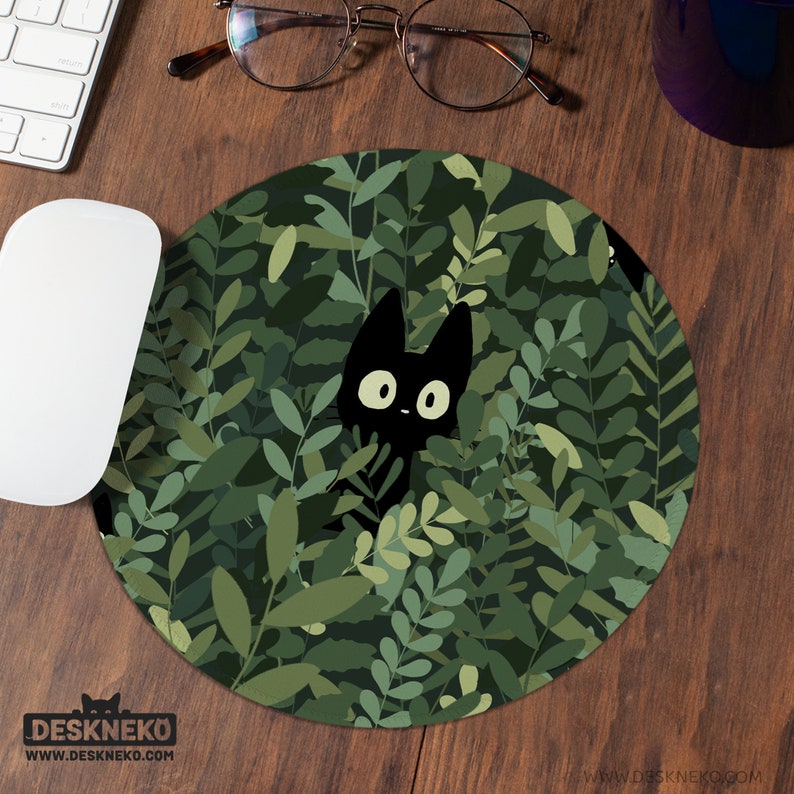 K&ouml;nnte beinhalten: Rundes Mauspad mit einer schwarzen Katze, die durch gr&uuml;nes Laub sp&auml;ht. Das Mauspad hat ein Muster aus dunkelgr&uuml;nen und hellgr&uuml;nen Bl&auml;ttern. Der Markenname "DESKNEKO" ist unten links aufgedruckt.