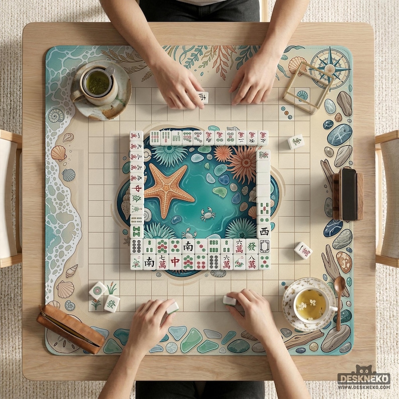 May include: A square wooden mahjong table with a beach-themed design, featuring a central ocean scene with a starfish. The game is in progress, with tiles and cups of tea visible. The table has the text "DESKNEKO" and "WWW.DESKNEKO.COM" on the bottom right.