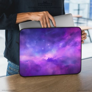 Puede incluir: Una funda para portátil con un diseño de nebulosa en tonos morados, azules y rosas. La imagen muestra un portátil parcialmente insertado en la funda, con un cierre de cremallera. El texto "DESKNEKO" es visible.