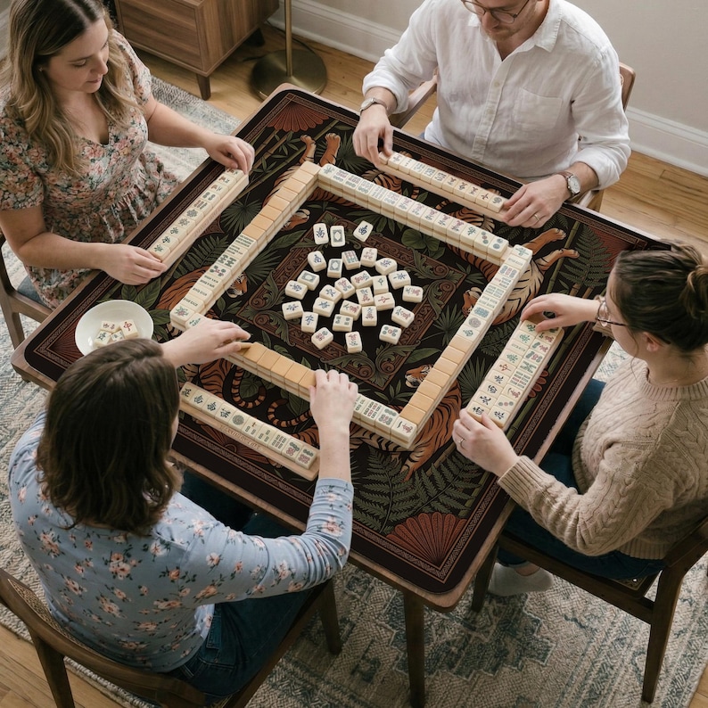 May include: A group of four people playing Mahjong around a brown table. The table has a decorative surface with a tiger and leaf pattern. The game pieces are beige with black markings.