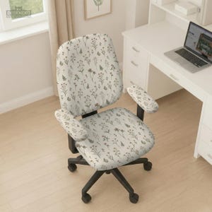 May include: An office chair with a cream-colored floral pattern. The chair has a black base with wheels and armrests. The floral design includes small flowers and leaves in shades of brown, green, and pink.