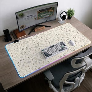 Pu&ograve; includere: Un grande tappetino da scrivania rettangolare con una superficie color crema e un delicato motivo botanico di sottili steli marroni, foglie e piccoli fiori. Il tappetino presenta una striscia luminosa a LED integrata lungo il bordo, che brilla di blu.