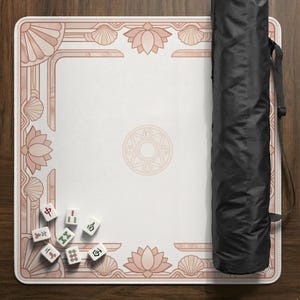 May include: A Mahjong game mat with a white center and a pink floral and seashell border. A black carrying case is on the right. Several Mahjong tiles are scattered on the mat.