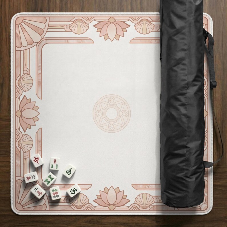 May include: A Mahjong game mat with a white center and a pink floral and seashell border. A black carrying case is on the right. Several Mahjong tiles are scattered on the mat.