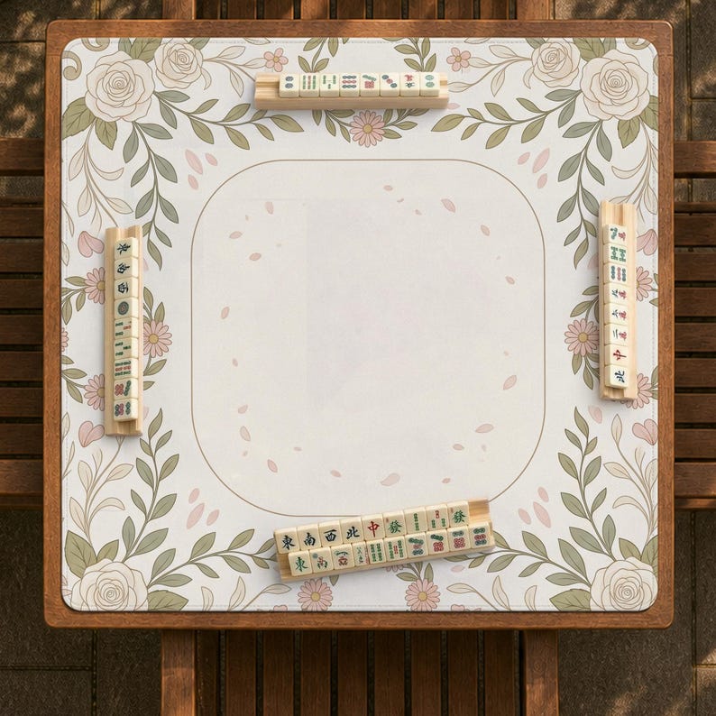 May include: A square mahjong mat featuring a white center with scattered pink petal illustrations, bordered by a floral pattern of roses, leaves, and small daisies. Four wooden racks hold mahjong tiles with various characters and symbols.