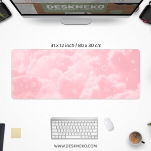 May include: Aesthetic desk mat with a pink cloud design and white celestial illustrations. The mat measures 31 x 12 inches. The website address www.deskneko.com is printed at the bottom. The mat is surrounded by a keyboard, mouse, and other desk accessories.