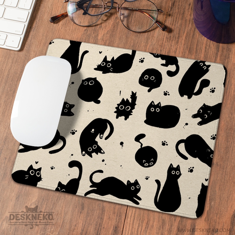Puede incluir: Una alfombrilla de rat&oacute;n rectangular beige con un patr&oacute;n repetido de ilustraciones de gatos negros y huellas de patas. Un rat&oacute;n de ordenador blanco descansa sobre la alfombrilla. La alfombrilla tiene el texto "DESKNEKO" y "Aesthetic Desk Mats with Funny Cats."