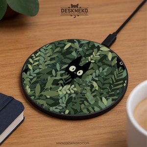 Puede incluir: Cargador inalámbrico redondo negro con un diseño de hojas verdes y un gato negro asomándose entre las hojas. El cargador tiene el texto "DESKNEKO" y "Aesthetic Desk Mats and Mouse Pads". La dirección del sitio web "WWW.DESKNEKO.COM" también es visible.